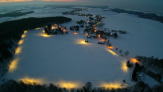 Schneelandschaft bei Sonnenuntergang und beleuchteten Wegen von oben fotografiert.