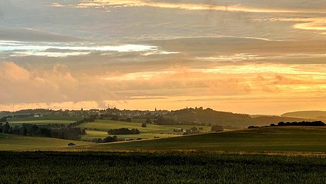 Die LEADER-Region ist als grüne hügelige Landschaft und wolkigem Himmel zu sehen. Im Hintergund Hartmannsdorf-Reichenau.