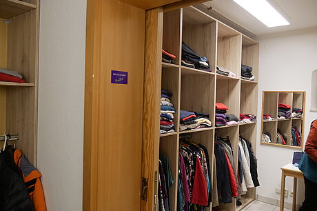 Raum mit mehreren Regalen, in welchen sich Kleidungsstücke befinden.