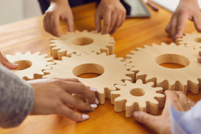 Zwei Hände, die 6 Tahnräder auf einem Tisch zusammenschieben.